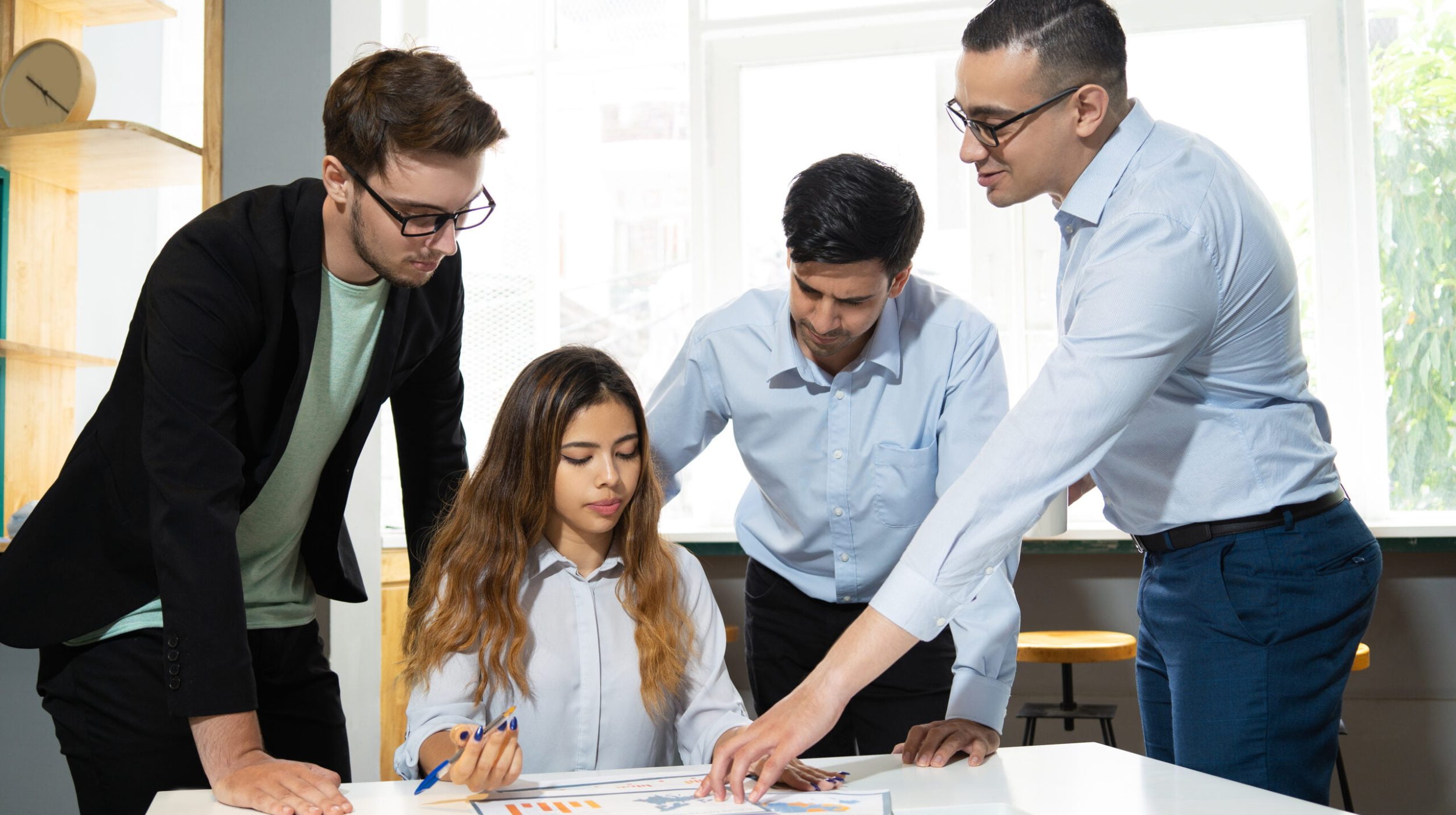 Mentor explaining marketing data interns. Confident office worker showing diagram to three pensive and focused colleagues. Mentorship concept